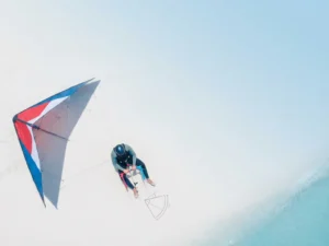 Beginnende kitesurfer met rode vlieger en controlestang op wit zandstrand, turquoise water en blauwe lucht op achtergrond