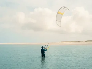 Beginnende kitesurfer in kalm turquoise water houdt gele controlebar vast terwijl kite rustig zweeft boven strand