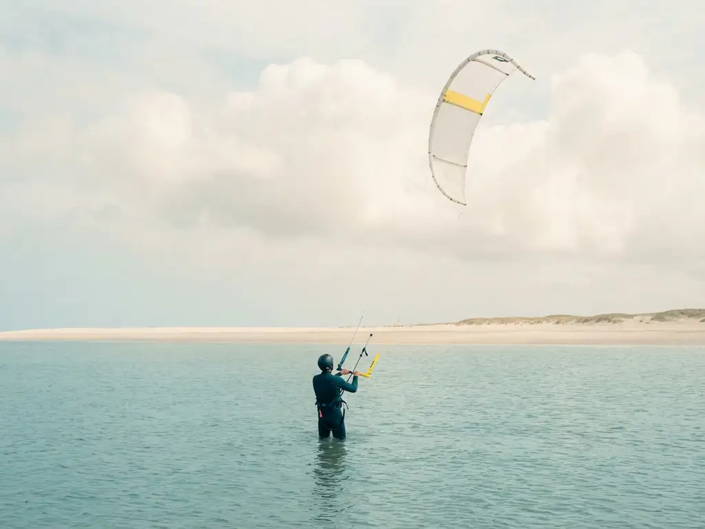 Beginnende kitesurfer in kalm turquoise water houdt gele controlebar vast terwijl kite rustig zweeft boven strand