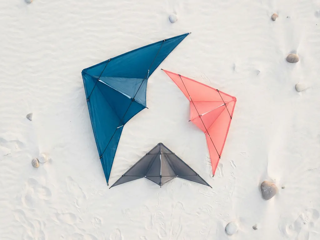 vliegers-strand-geometrisch-minimalistisch-design.jpg Drie premium vliegers in oceaanblauw, koraalrood en antracietgrijs gerangschikt in driehoekige formatie op wit zand
